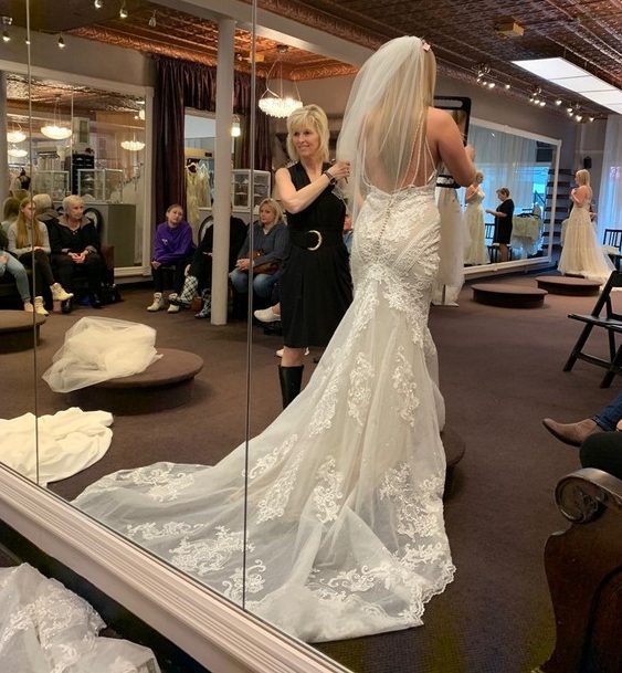 Bride trying on dress with bridal stylist in bridal shop