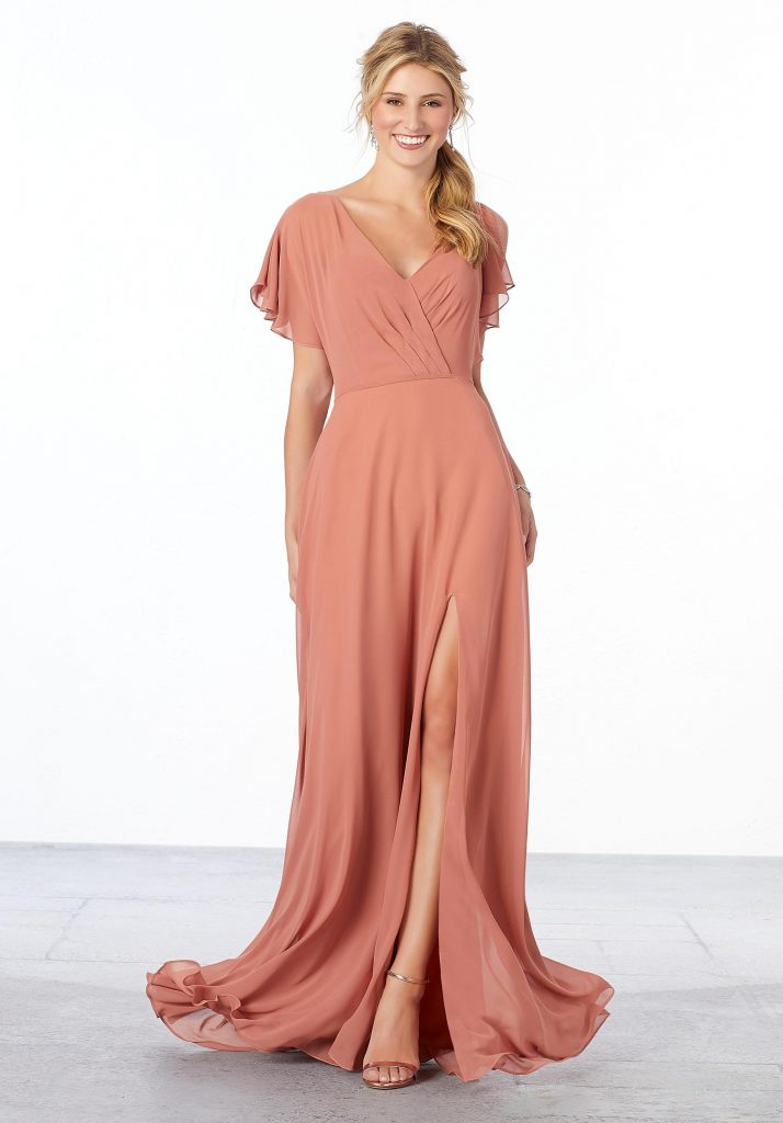 Young woman wearing flowing spice-colored A-line chiffon bridesmaid dress featuring a surplice bodice with flutter sleeves, v-back, and front slit